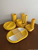 Overview of full yellow melamine dish set showing divided plates, cups, bowls, trays, salt and pepper shakers, and corn holders