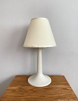 Vintage white table lamp against plain light background, unlit, showing full lamp from base to shade