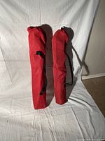 Two red carry bags containing folding pole camp chairs, shown standing upright against a white background.