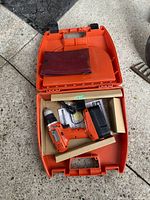 Black & Decker cordless drill inside the orange carrying case with charger and manual/pouch.