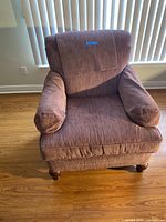 Front view of burgundy upholstered armchair, showing cushioned seat, padded armrests, and wooden legs on hardwood floor against blinds.