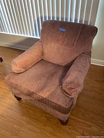 Burgundy fabric armchair with cushions and wooden legs shown in natural light on wooden floor.