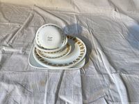 Photo showing stacked Corelle dishes including square plate at bottom and round plates and bowls stacked on top, displaying the golden floral pattern.