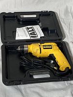 Yellow DeWalt electric drill with corded power supply inside black plastic carrying case, showing tool, case, and instruction manual