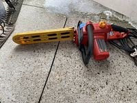 Side view of the Homelite electric chainsaw with yellow blade guard and power cord on concrete floor.