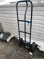 Front view of black metal hand truck cart with two large pneumatic tires and wide base plate for carrying items.