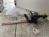 Full view of green Black & Decker electric hedge trimmer with visible cutting blade, black handles, and power cord.