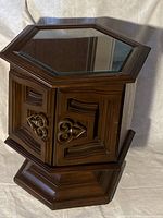 Full view of hexagonal end table showing walnut finish, raised base, clear glass inlay, and carved door panels