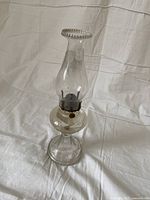 Front angle view of the clear glass hurricane lamp placed on a white fabric background.