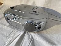 Front and side view of the silver KOSS portable entertainment system showing speakers, cassette tape deck, and control buttons.