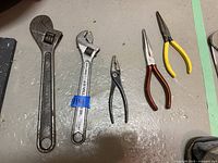 Two adjustable wrenches, one wire cutter, and two needle nose pliers laid out on a cement floor.