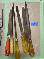 Six metal and wood files of different shapes and sizes with plastic handles in red, yellow and clear yellow shown against a gray background.
