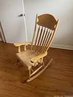 Side view of the maple/oak finished wooden rocking chair showing seat, armrest, curved rocker rail and backrest.