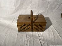 Closed view of walnut finish fold-out sewing basket with central handle and diagonal accents on sides.