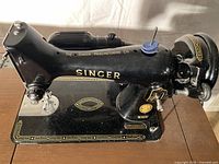 Close-up side view of vintage black Singer electric sewing machine showing gold logos and detailing, mounted on a wooden base.