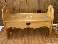 Front view of small wooden bench, showing heart cutout detail and handles.