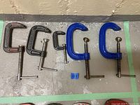 Five metal C clamps of varying sizes and brands laid out on the floor.
