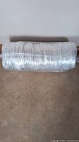 Roll of flexible insulated air ducting lying on floor, wrapped in plastic.