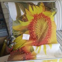 Fabric sunflower printed screen with large flower face, detailing petals, center and green leaves. Fabric laid over chair with metal hanging bar.