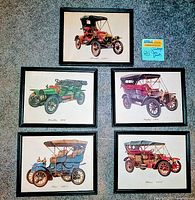 Set of five framed antique car prints arranged on floor, showing each black wood frame and colorful vintage car illustrations.
