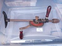 Photo shows side view of vintage manual chest drill press with wooden handles, metal crank, round gear, and metal chest plate base.