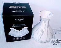 Photo of the diffuser alongside its original black packaging box. Box states features 7 color changing LED light, ultrasonic waves, and timer function.