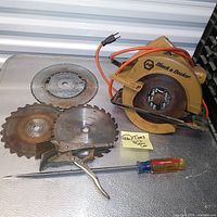Lot contents showing Black & Decker circular saw with power cord, three circular saw blades, Peterson Vise Grip and Craftsman screwdriver laid on metal surface.