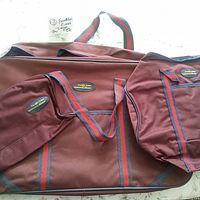 Three brown cloth Franklin Evans Collection travel bags: wardrobe, duffle and toiletries, with red and dark gray striped handles, shown together