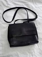Photo of black leather Nine West crossbody handbag laid flat, showing entire bag with strap and flap.