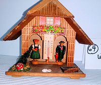 Full front view of wooden chalet style barometer thermometer weather station with figurines of girl and boy, mushroom, greenery and trough.