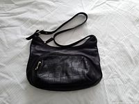 Full view of the black genuine leather shoulder handbag with adjustable strap and front zipper pocket.