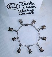 Full view of the sterling silver turtle charm bracelet laid flat on a white cloth, showing all ten turtle charms and magnetic clasp connected.