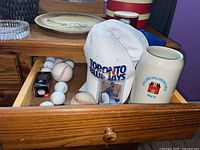 Shot of open drawer with baseballs, golf balls, two baseball caps, Jose Reyes baseball card and Feldschlosschen Bier stein on a wooden dresser