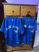 Two blue Toronto Blue Jays jerseys hanging from single chest drawer knob, shown full front view.