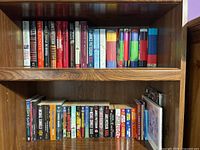 Two shelves of books showing multiple novels including hardcovers and paperbacks in various colors and titles.