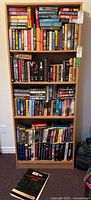 Full view of wooden bookshelf with four shelves filled with varied hardcover and softcover books.