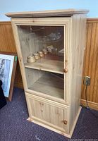 Front angled view of veneer media cabinet showing glass front door upper compartment and lower solid door compartment with wood knobs