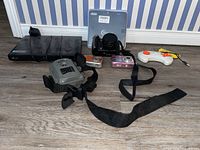Lot items arranged on floor showing LG Blu-ray player, Simmons trail camera with strap, three digital cameras, Blast game controller.
