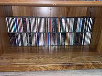 Full view of the bottom wooden shelf showing the collection of CDs arranged side by side.