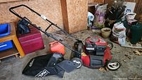 Red Craftsman lawnmower with foldable black handle, grass collection bag attached, and empty red gas can on the ground beside in a garage setting.