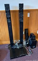 Photo of the overall home theater system including two tall tower speakers, center speaker, subwoofer, satellite speakers, Blu-Ray player on floor with wiring and remote control.