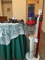 Full view of Dyson Cyclone V10 Motorhead vacuum with charging stand and multiple attachments laid out on a table nearby. Vacuum is upright on the charging stand which is white.