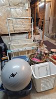 Photo shows the metal drying rack with three fabric compartments, several wicker baskets, plastic bins, and the silver exercise ball in a basement setting.