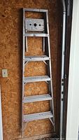 Ladder folded and leaning against a plywood wall in the garage, showing full height and step arrangement.