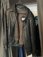 Front view of black Ports International leather jacket hanging on a hanger, showing buttons, collar, and inner patterned lining.