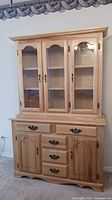 Full view of pine buffet and hutch set placed against a wall, showing natural wood finish and glass doors on hutch.