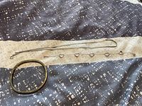 Photo showing the three pieces: thin snake chain necklace, heart-link bracelet, and bangle bracelet on fabric.