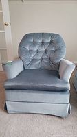 Front view of light blue velvet tufted armchair with skirted base and removable cushion.