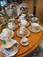 Overview of all 12 teacups with 11 saucers and 3 collector plates arranged on a wooden table.