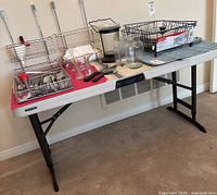 Full side view of white rectangular utility table with black adjustable legs and various kitchen items placed on top (not included in lot)